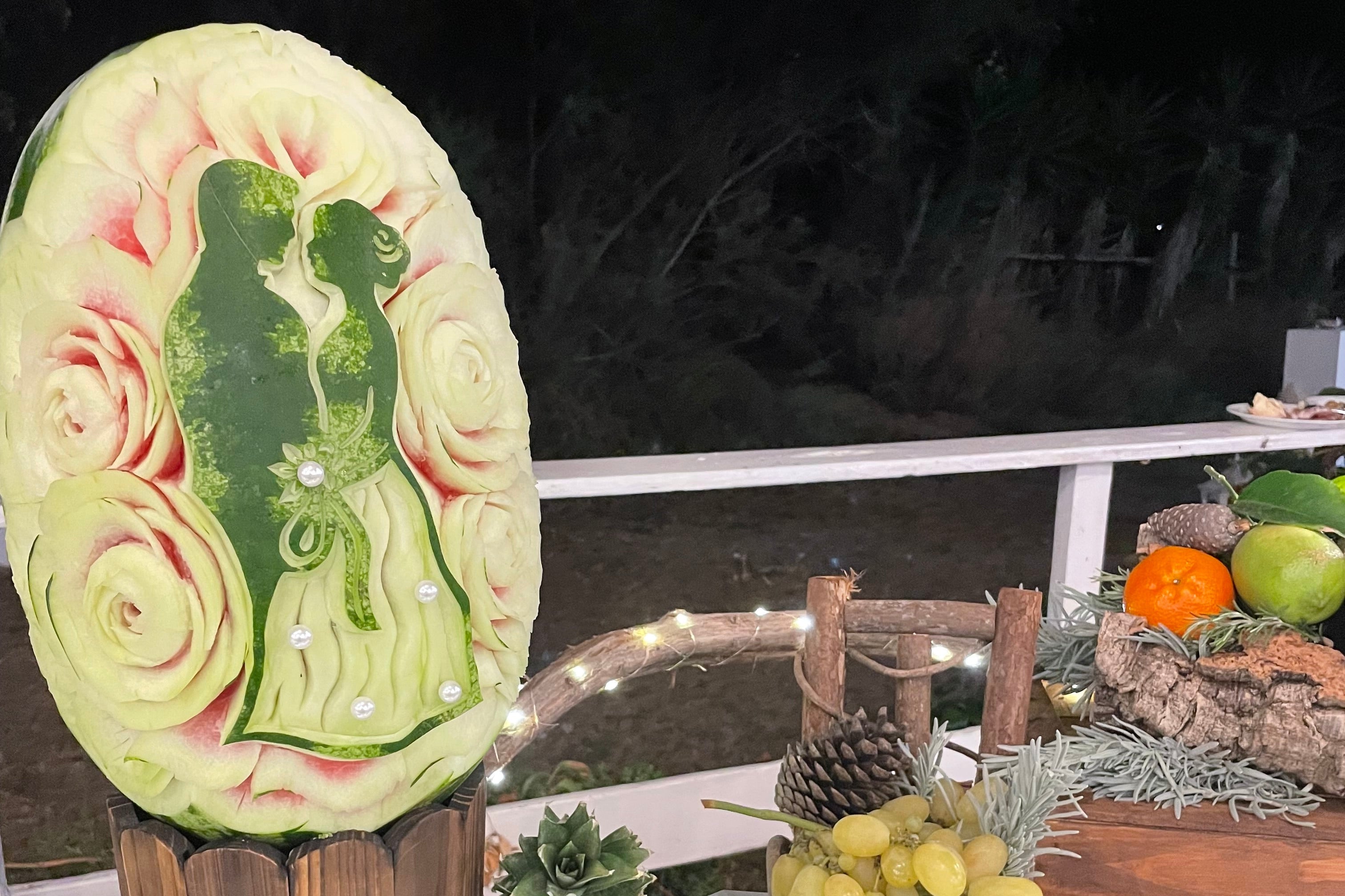 Scultura su anguria con silhouette degli sposi tra rose intagliate a mano per buffet matrimoniale in Sardegna